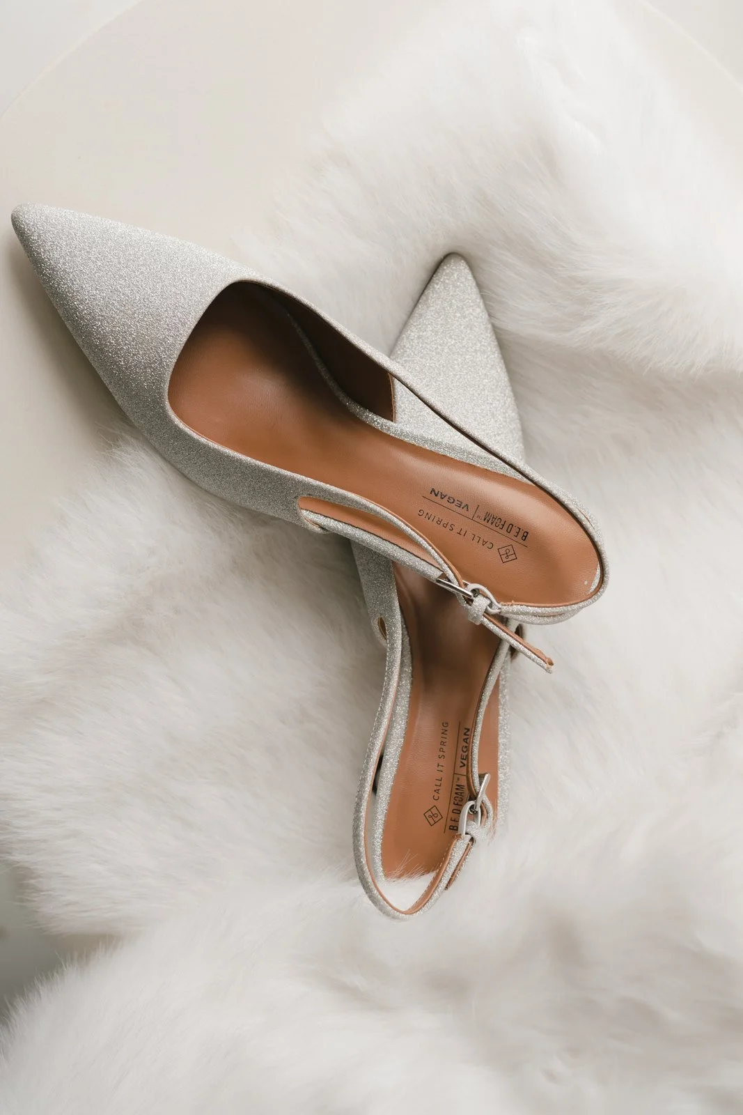 Silver glitter high-heeled shoe resting on a white fur surface.