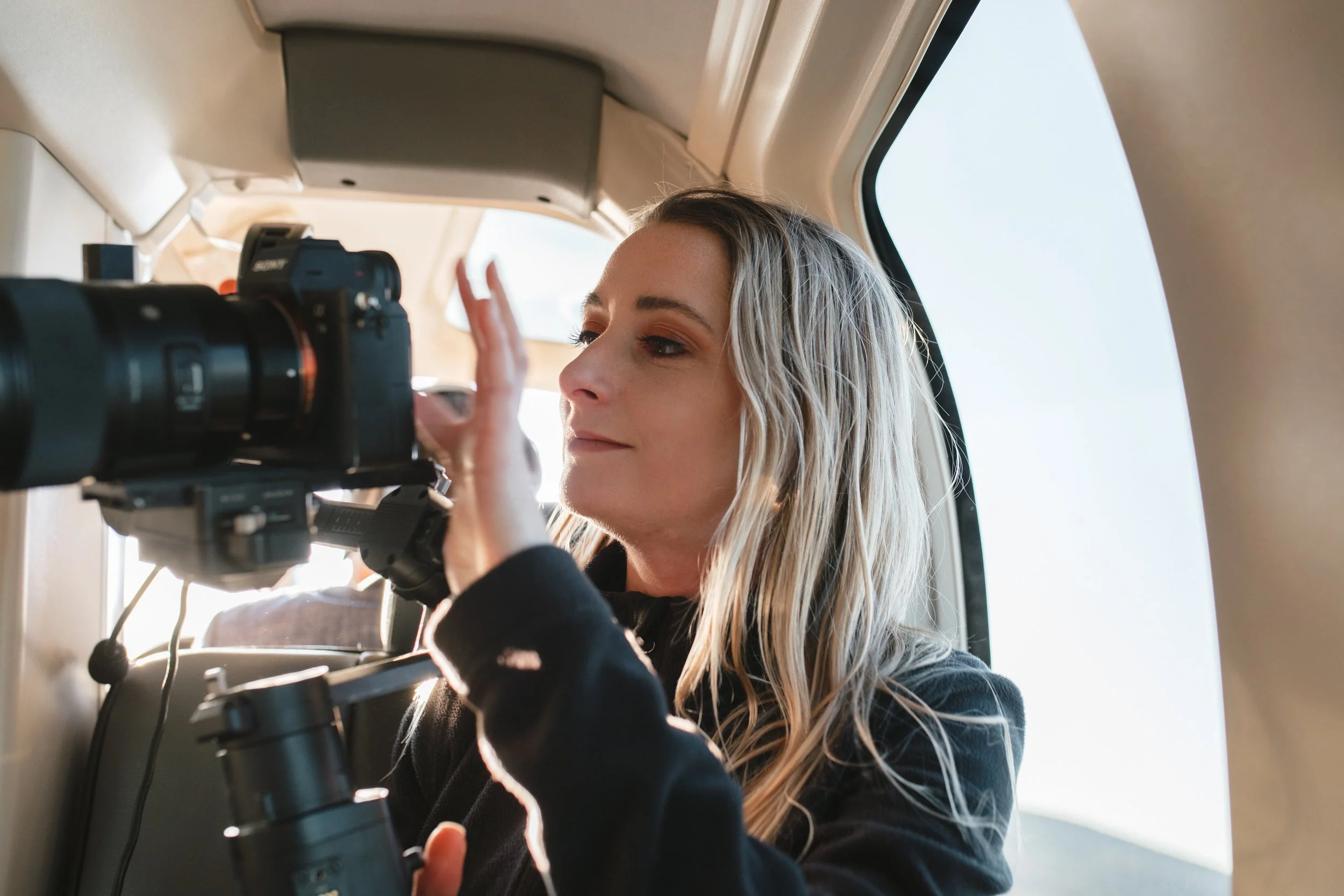 A woman looking through a camera's viewfinder in a helicopter, with sunlight illuminating her face. Gqeberha wedding photographer and videographer