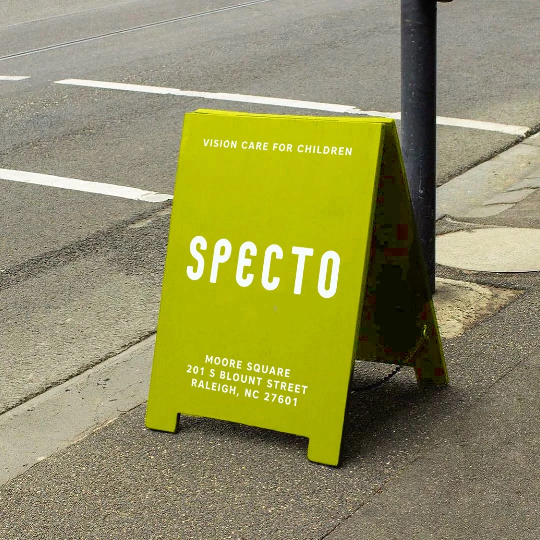 Bright yellow sidewalk sign with white text for Specto, located at Moore Square in Raleigh, North Carolina.