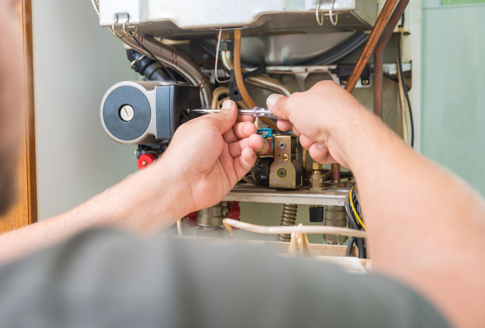 Close-up of a technician's hands repairing or maintaining an industrial or mechanical device with various pipes, wires, and components.