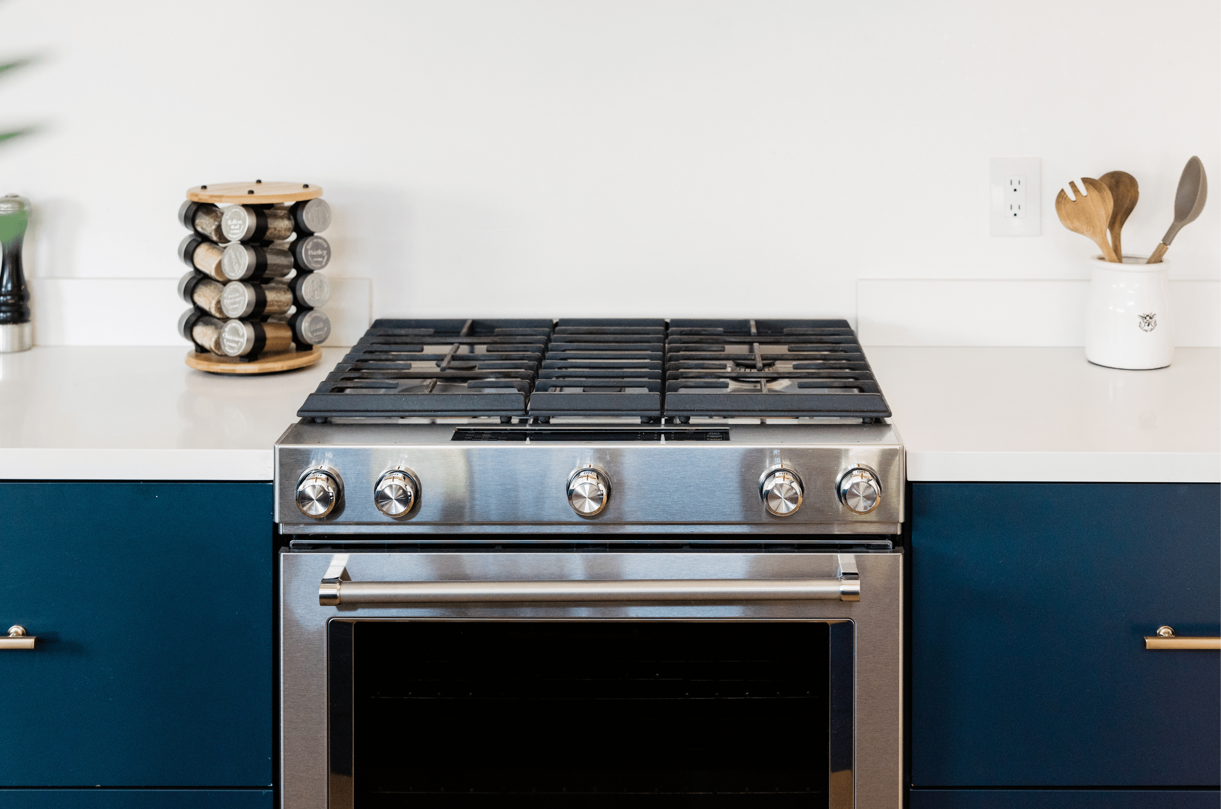 Modern kitchen with stainless steel stove, blue cabinetry, spice rack, and white countertop with kitchen utensils.