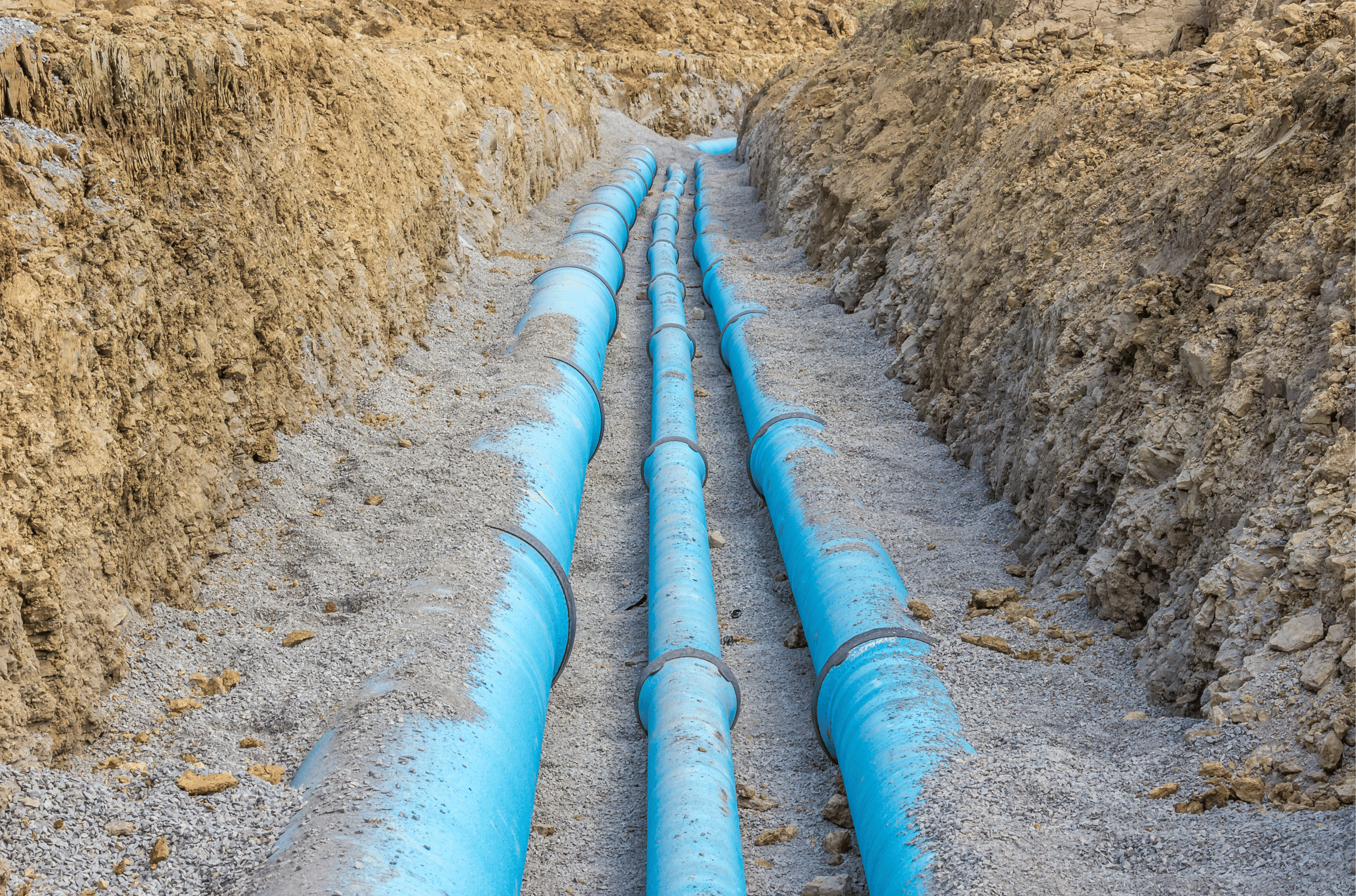 Three large blue pipes laid in a trench with dirt and rocks on the sides.