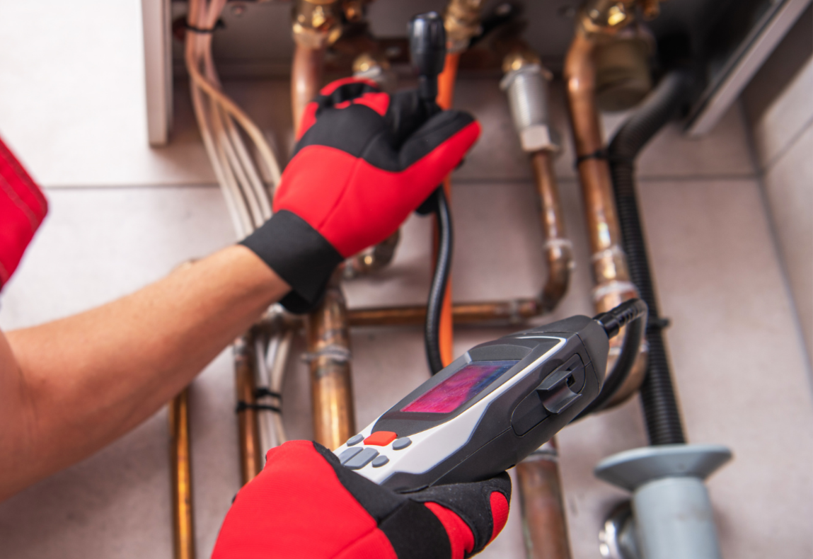 Technician wearing red gloves inspecting copper plumbing pipes with a diagnostic tool.
