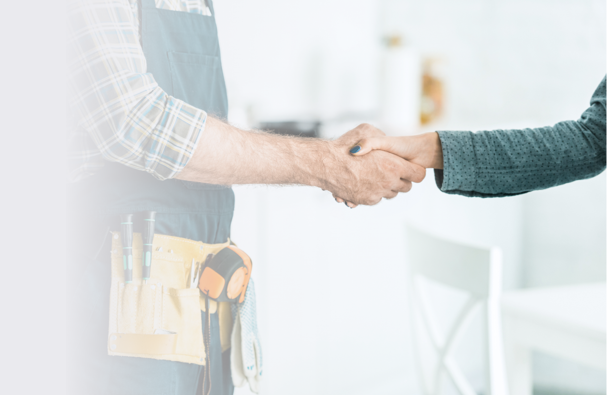 Two people shaking hands, one wearing a plaid shirt and tool belt, the other wearing a dark cardigan with small polka dots, in a well-lit room.