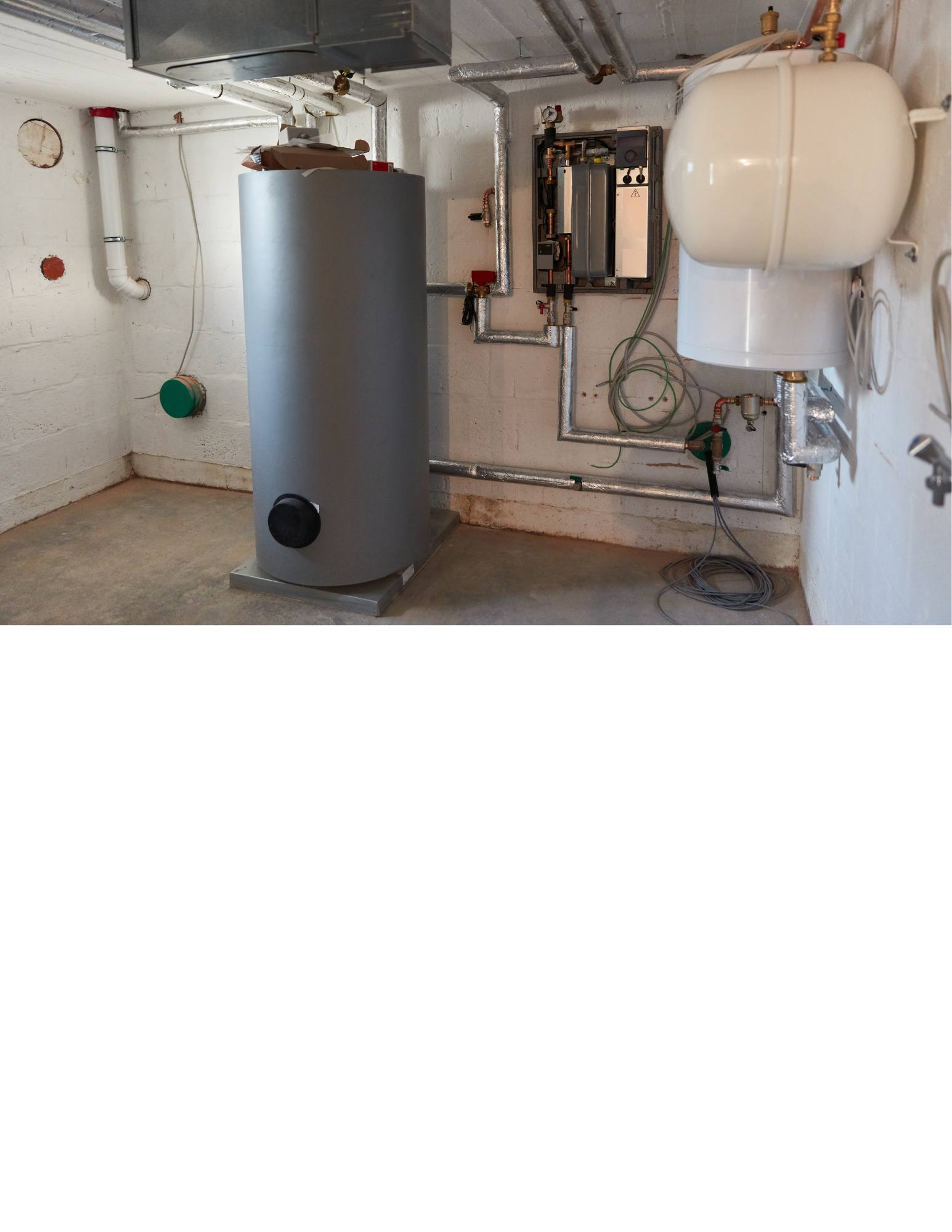 An industrial utility room with a large water heater, pipework, and a control panel mounted on the wall.