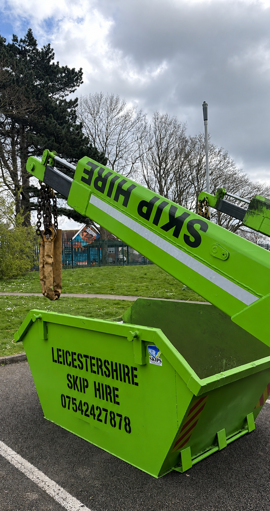 Green skip rental container with black text advertising LeicesterShire Skip Hire and phone number, with a crane arm labeled 'Skip Hire' positioned above it.