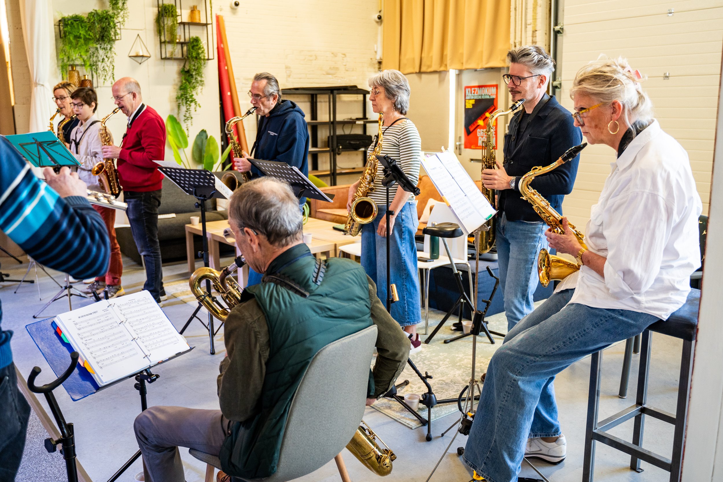 Mensen spelen saxofoon samen in een oefenruimte, sommigen staan terwijl anderen zitten.