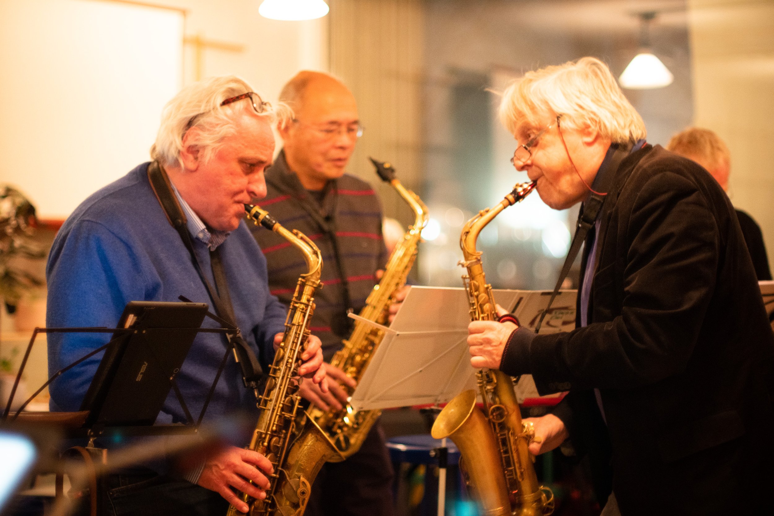 Mannen en vrouwen die samen jazzmuziek maken met saxofonisten, terwijl ze bladmuziek bekijken in een gezellige, warme sfeer.