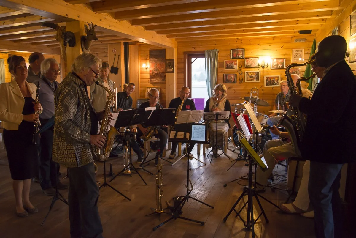Muziekkwartet met muzikanten die saxofonen, klarinetten en een drum bespelen in een houten kamer met foto's aan de muur.