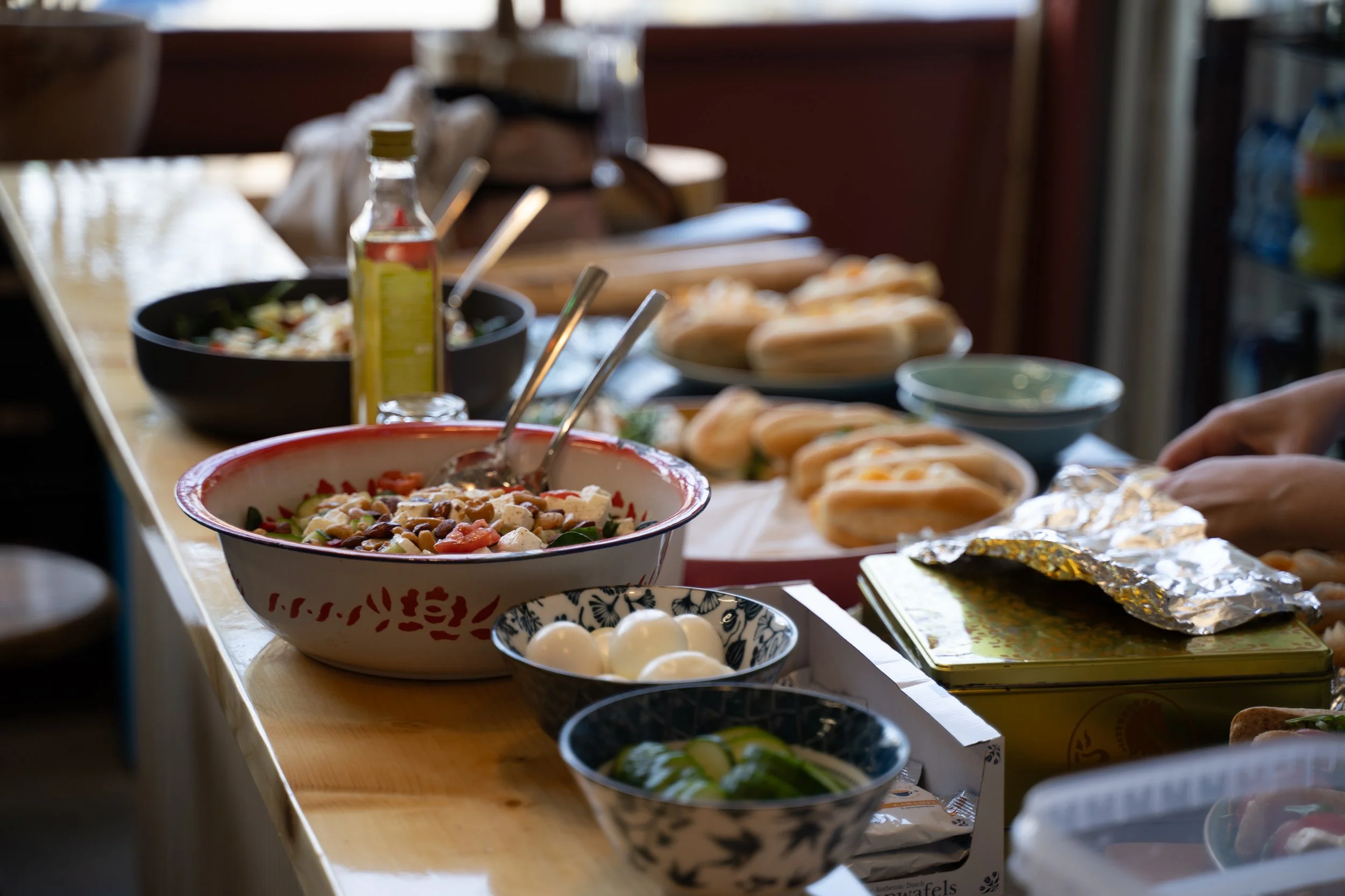 Verspreide tafel met diverse gerechten zoals salades, broodjes, eieren en sausflesjes in een gezellige keuken of eetruimte.