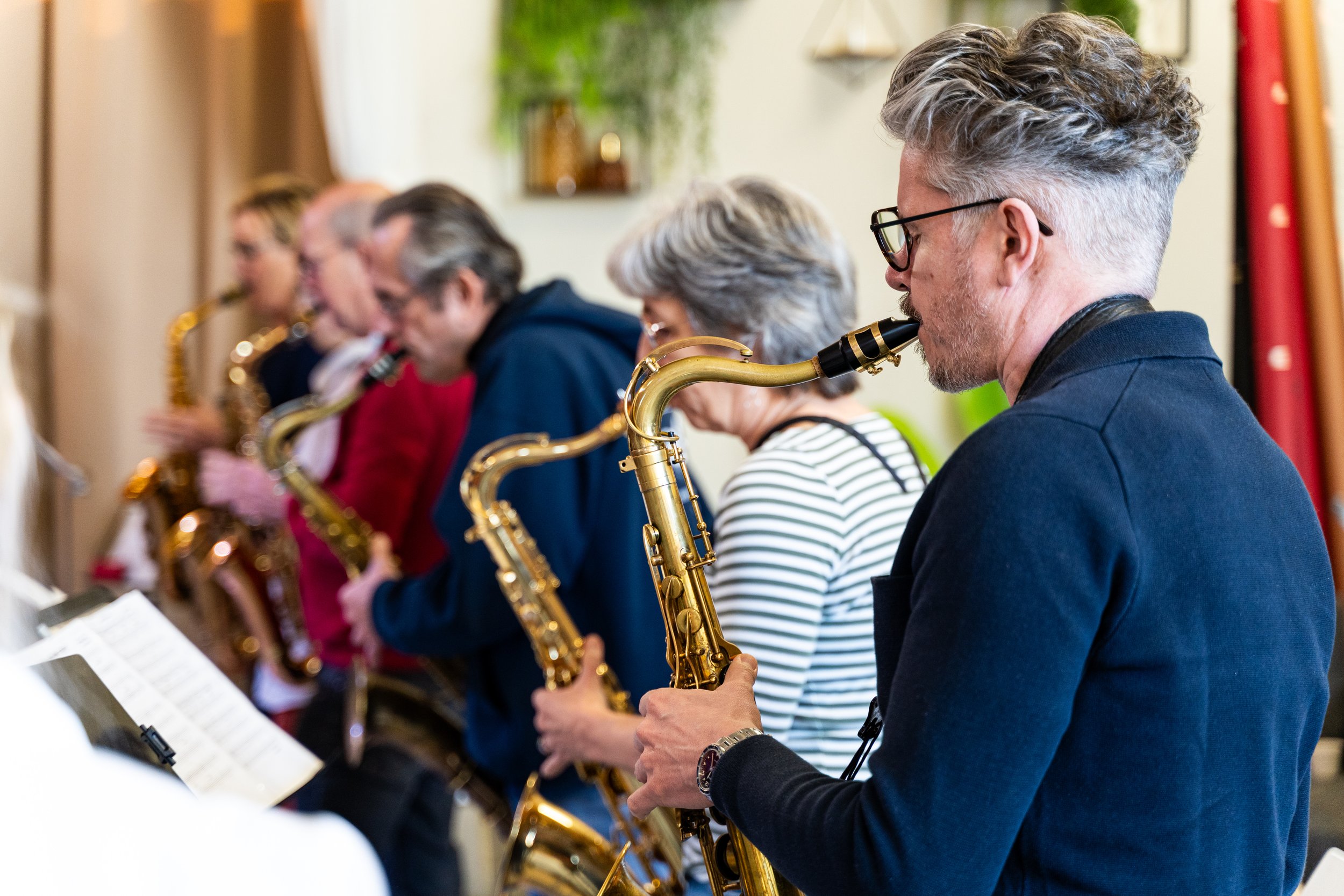 Mensen spelen saxofoon tijdens een ensembleoptreden in een kamer met groene en rode decoraties.