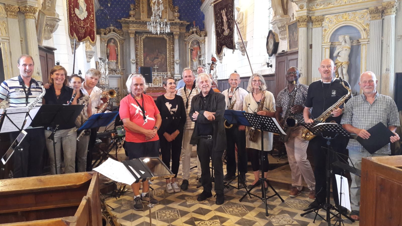 Groep muzikanten in een kerk, met allerlei instrumenten zoals saxofoons, klarinetten en een bas, poseert voor een groepsfoto.