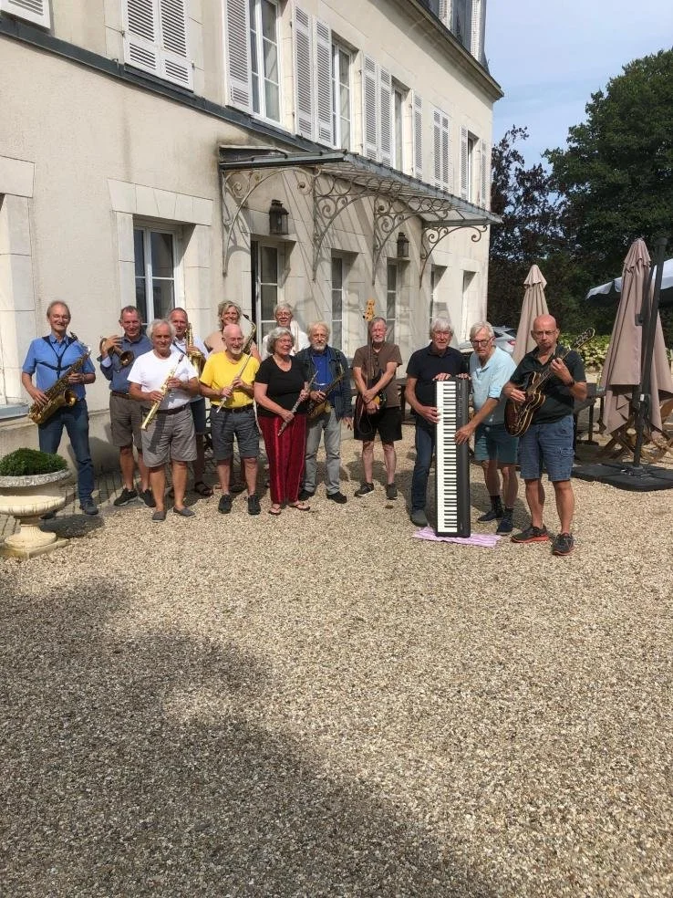 Een groep muzikanten staat buiten voor een witte klassieke villa, met instrumenten zoals saxofoon, gitaar en keyboard.