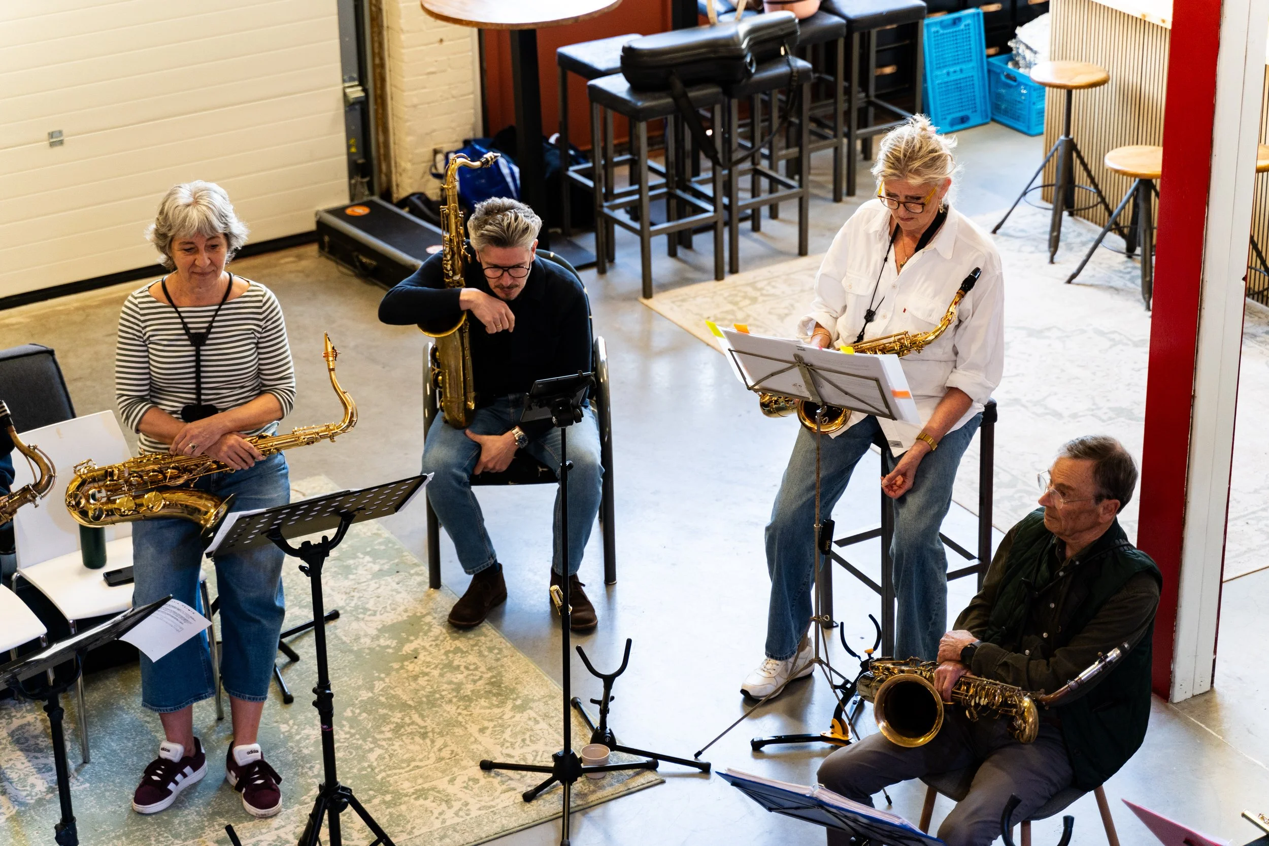 Mensen die samen muziek oefenen of optreden, met bladmuziek en saxofons op een repetitie of concert.