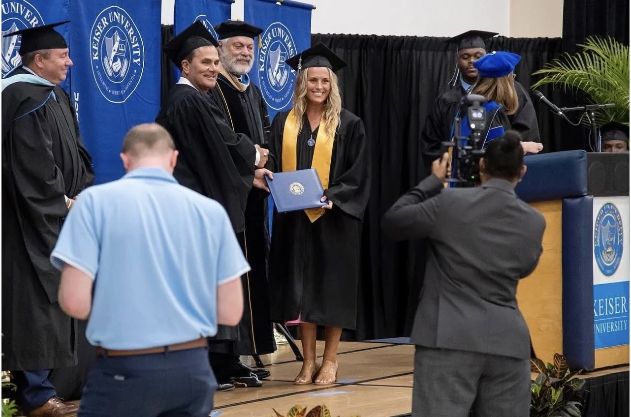 Graduation ceremony at Keiser University with graduates in caps and gowns, faculty, and staff on stage, and a photographer capturing the moment.