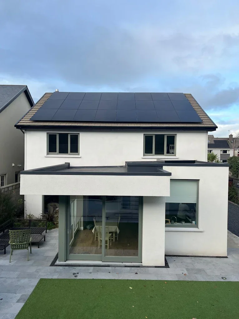 Modern house with solar panels on roof and large glass sliding door leading to backyard with patio furniture and artificial grass