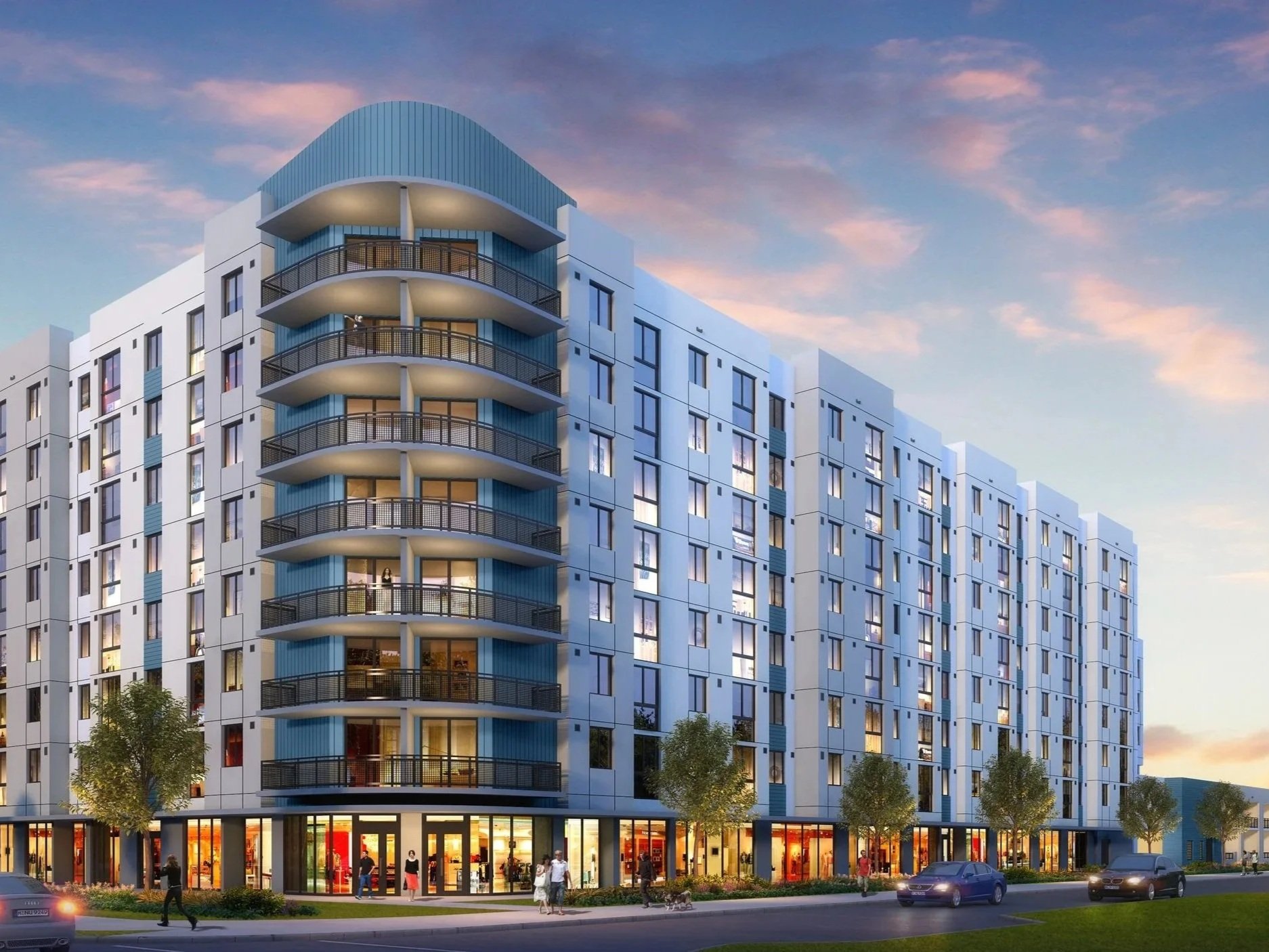 Modern multi-story residential building with curved balconies, large windows, retail shops on the ground floor, and people walking outside at dusk.
