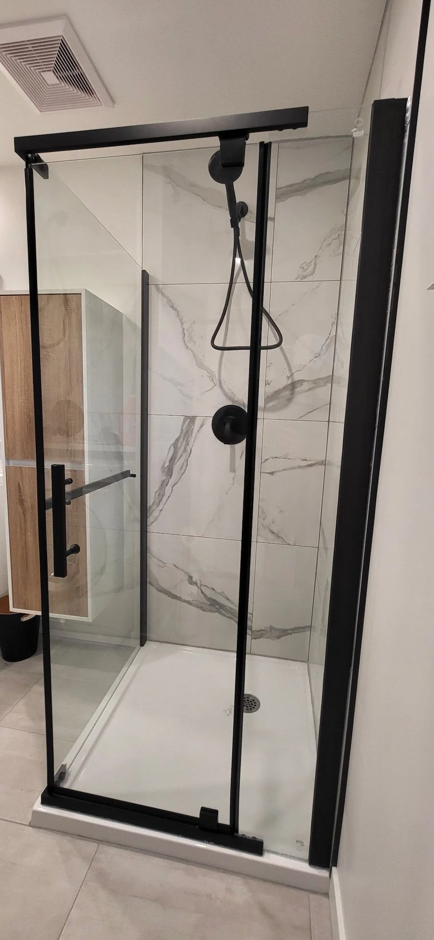 Cabine de douche avec mur en marbre, porte en verre et un pommeau de douche.