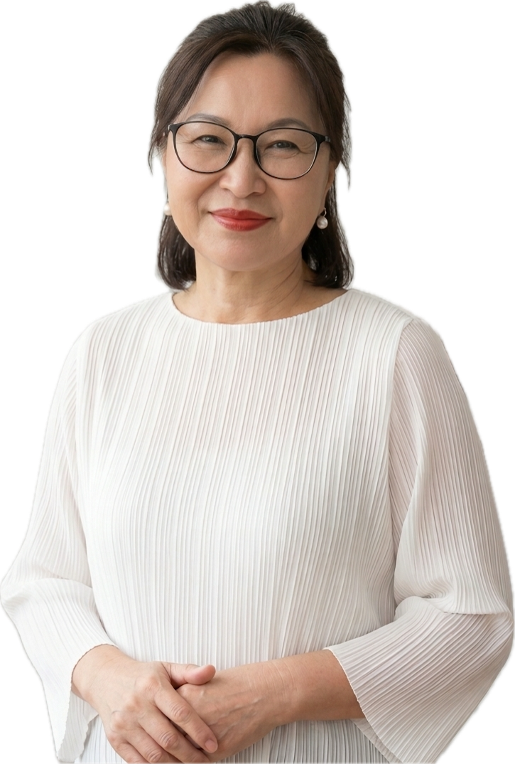 A middle-aged woman with glasses and shoulder-length dark hair, smiling, wearing a white pleated blouse, standing with hands clasped.