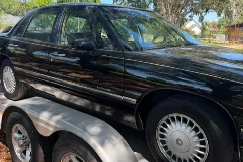 Black sedan car on a trailer that was towed to the garage.
