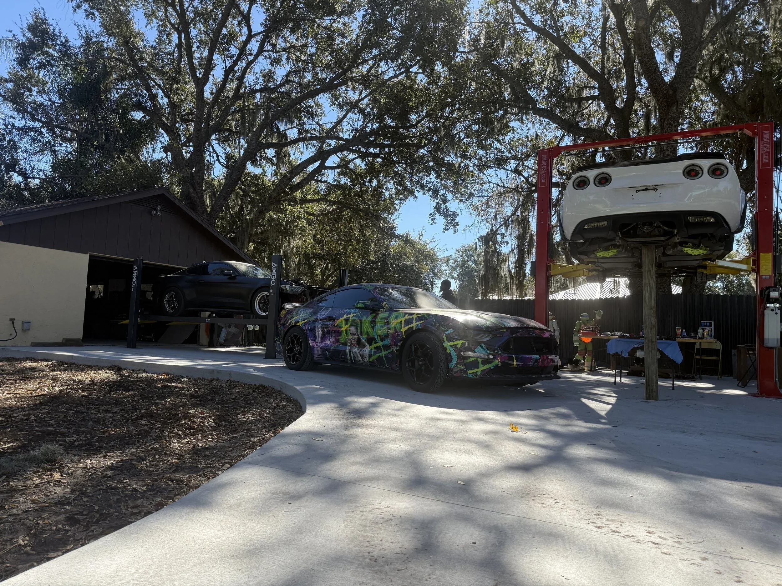 A car is lifted on a hydraulic lift at an auto repair shop. There are other cars and a person working in the background.
