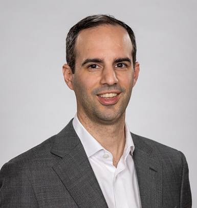 Professional man in gray suit with white shirt smiling at the camera.
