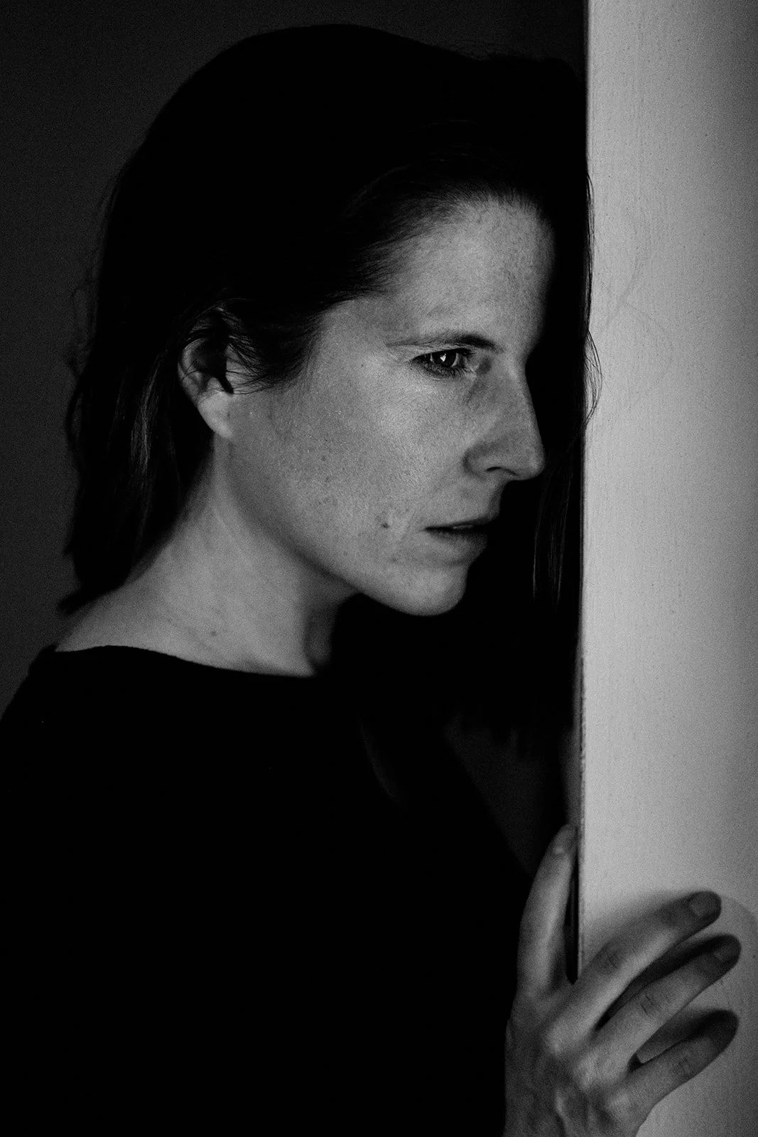 Black and white photo of a woman peeking from behind a wall, with a focused and intense expression.