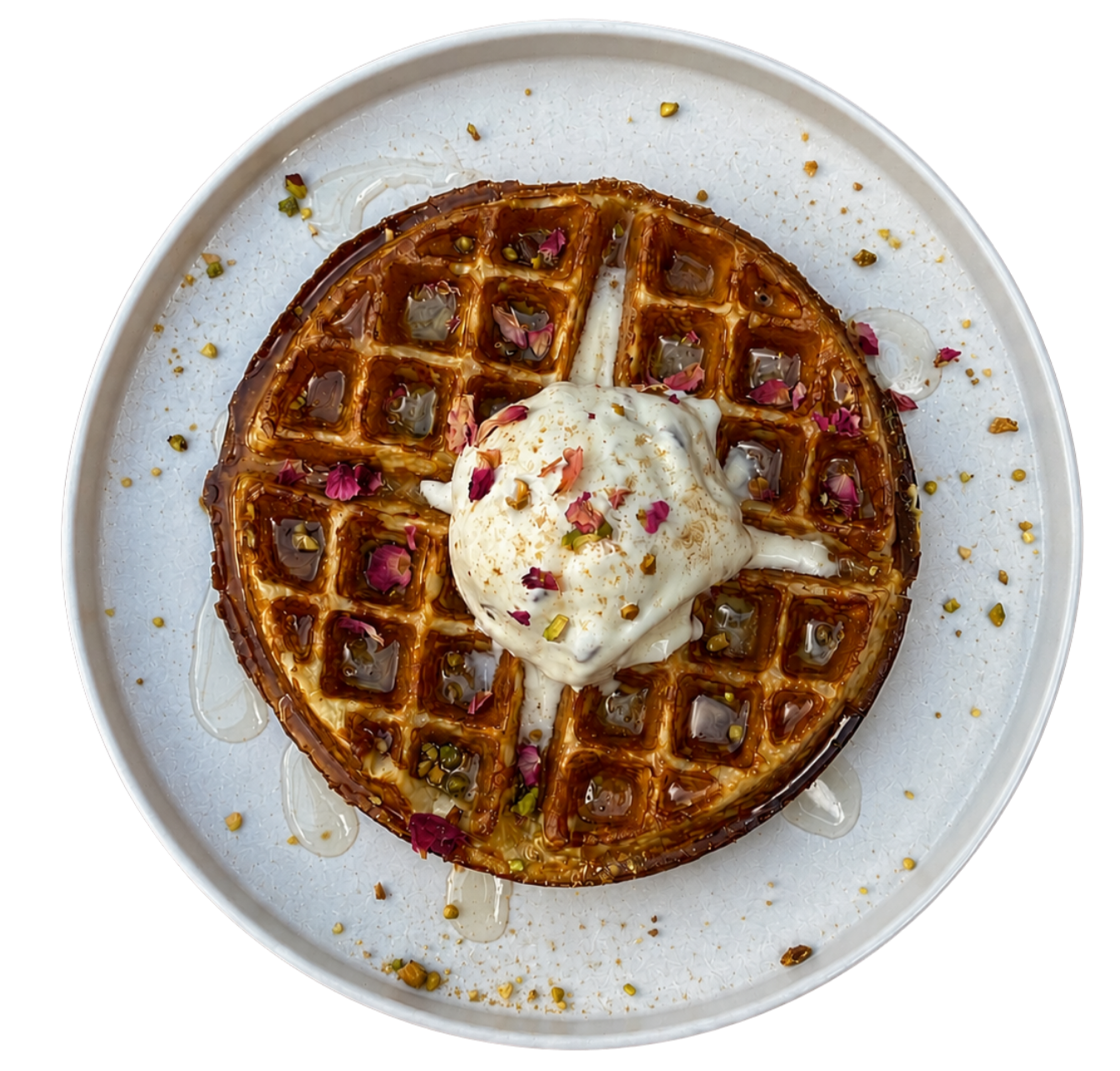 A plate of dessert waffles topped with whipped cream, pink flower petals, candied pistachios, and syrup drizzles.