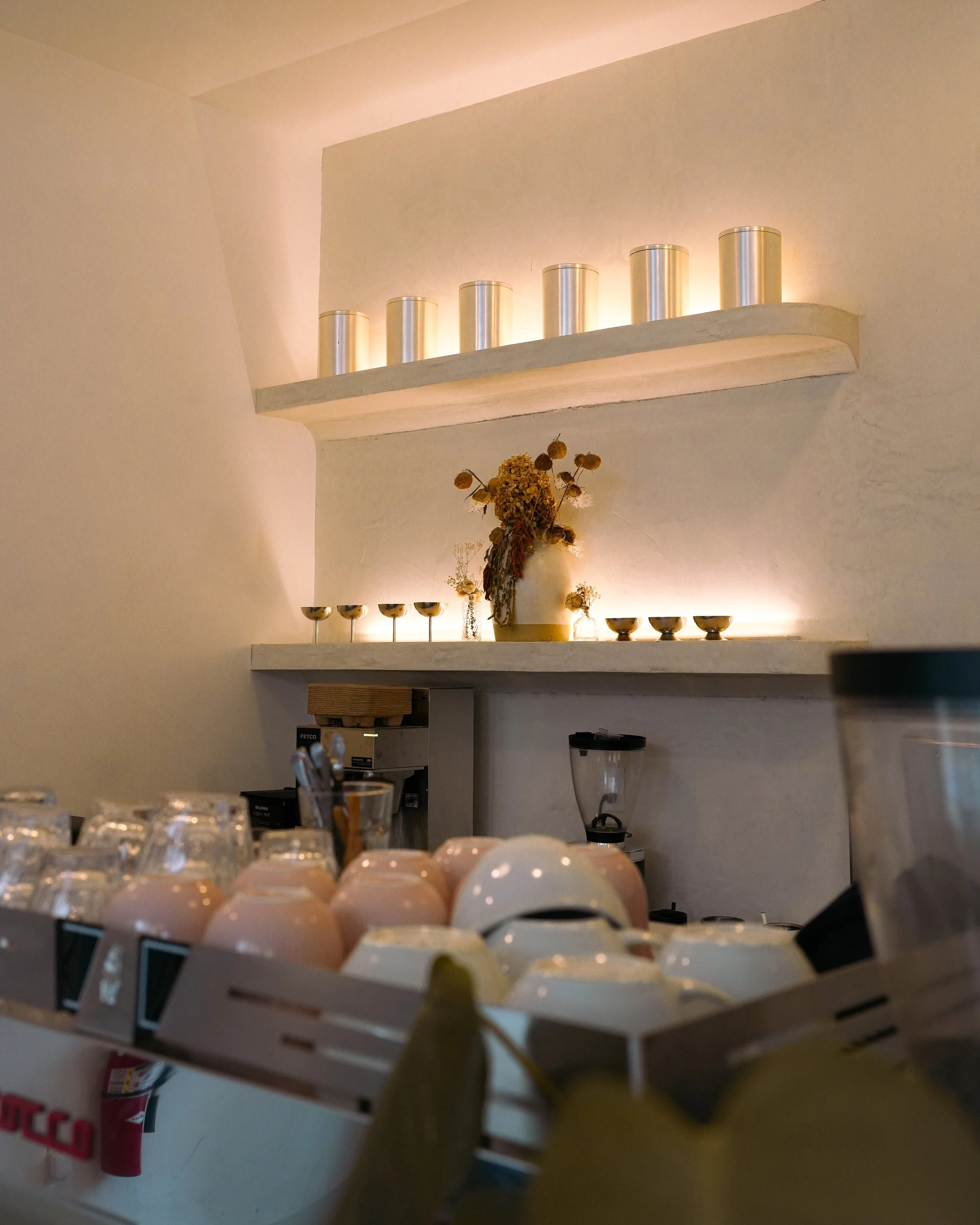 Wall shelves with metal cans and dried flowers, cups in foreground, kitchen items below.