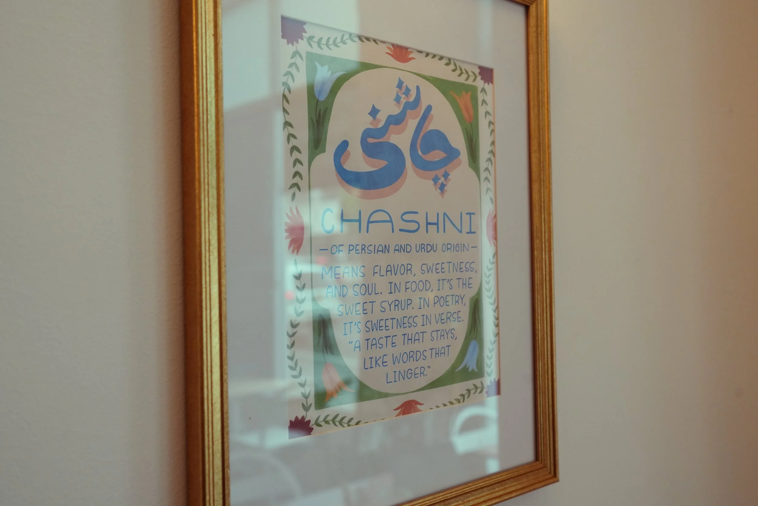 Framed decorative poster with colorful floral designs and the word 'Hashni' at the center, along with a description of its Persian and Urdu origin and meaning.
