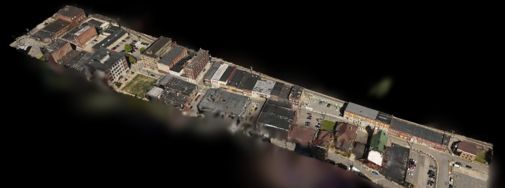 Aerial view of a city block with various commercial and residential buildings, streets, parking lots, and some green spaces.