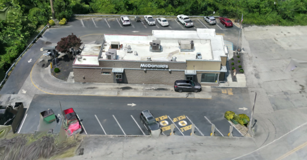 Aerial view of a McDonald's restaurant with parking lot and cars parked around it, surrounded by greenery.