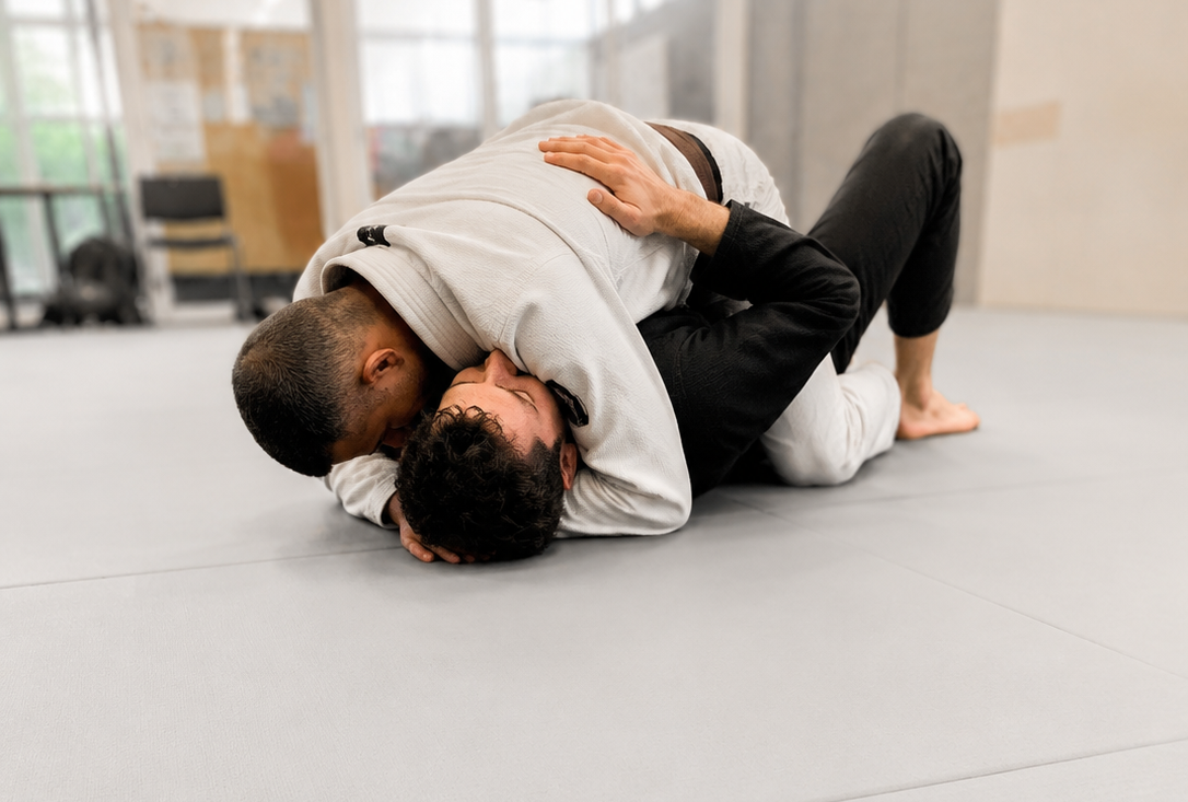 Deux personnes pratiquant le jujitsu ou le wrestling sur un tapis gris, en tenue de sport, dans une salle d'entraînement
