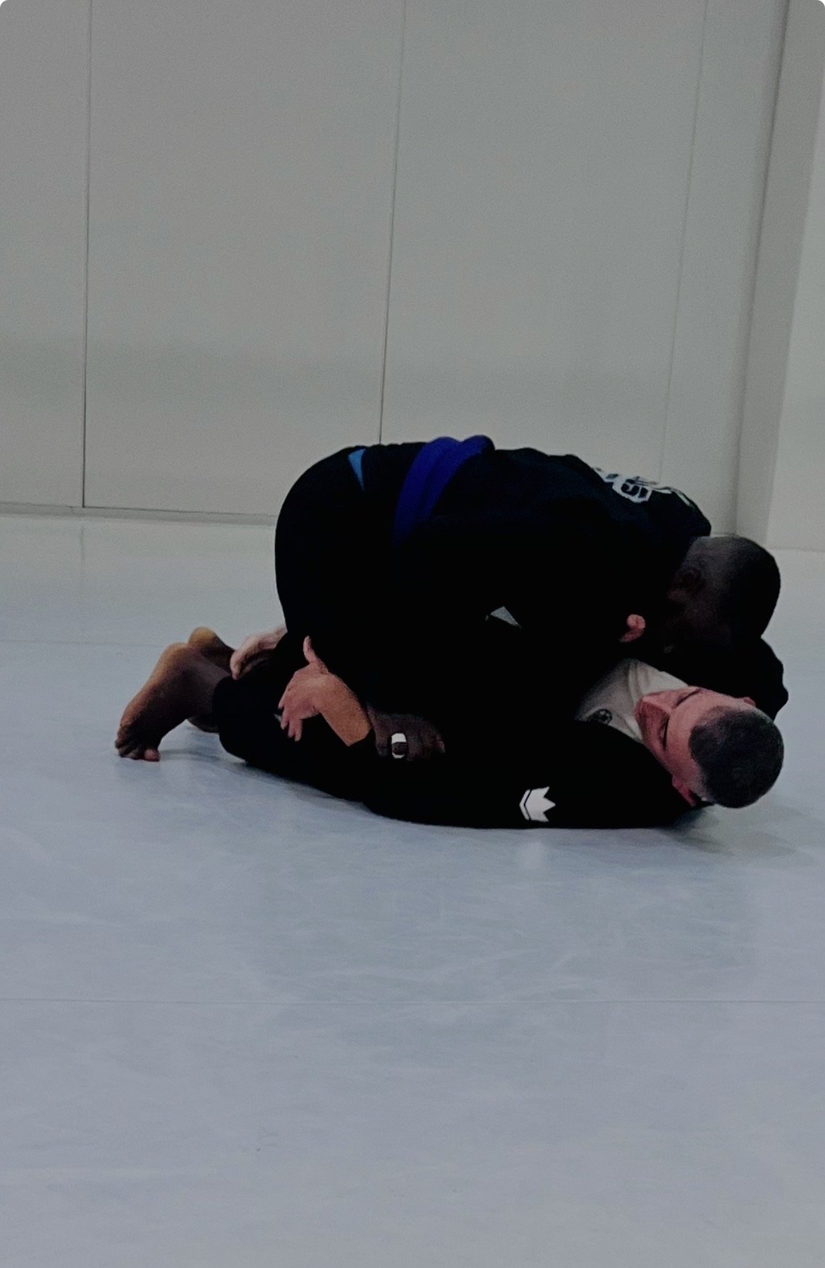 Deux personnes pratiquent le jiu-jitsu brésilien, une en position de soumission sur l'autre, dans une salle d'entraînement.