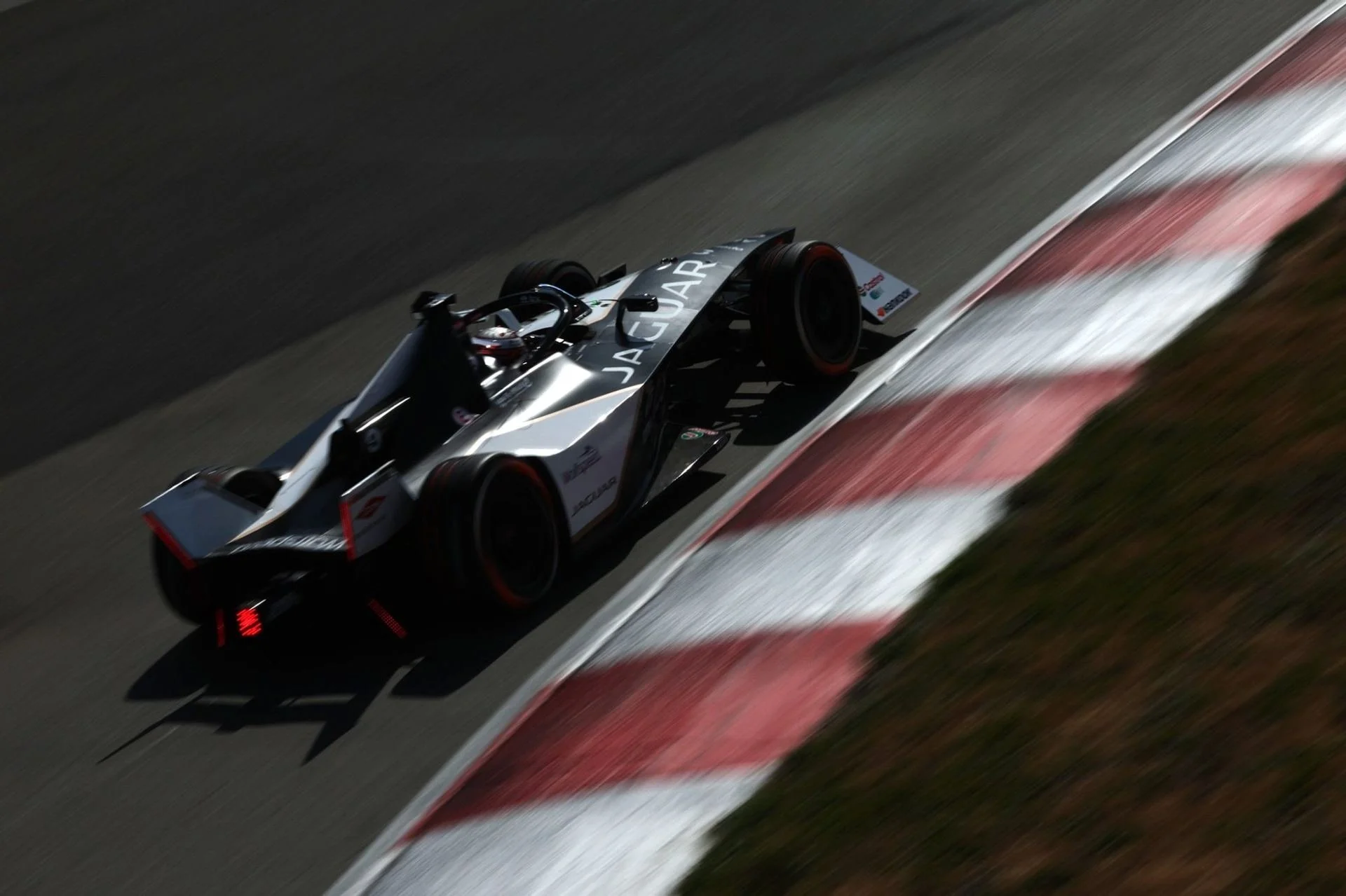 A race car on a race track taking a turn, with visible sponsor logos and red tire marks on the track surface.