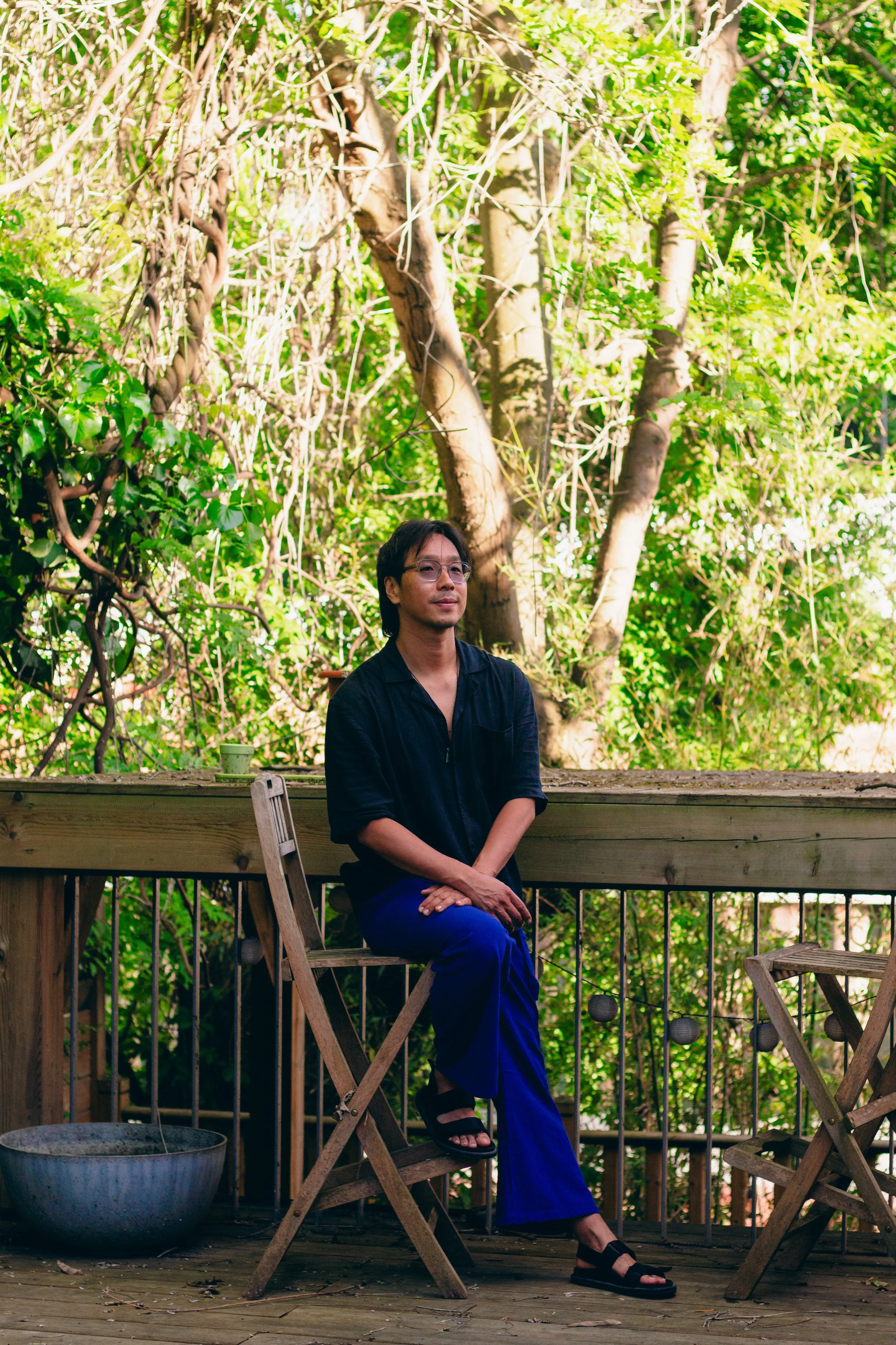Homme assis sur une chaise en bois sur un pont en bois entouré de verdure et d'arbres.