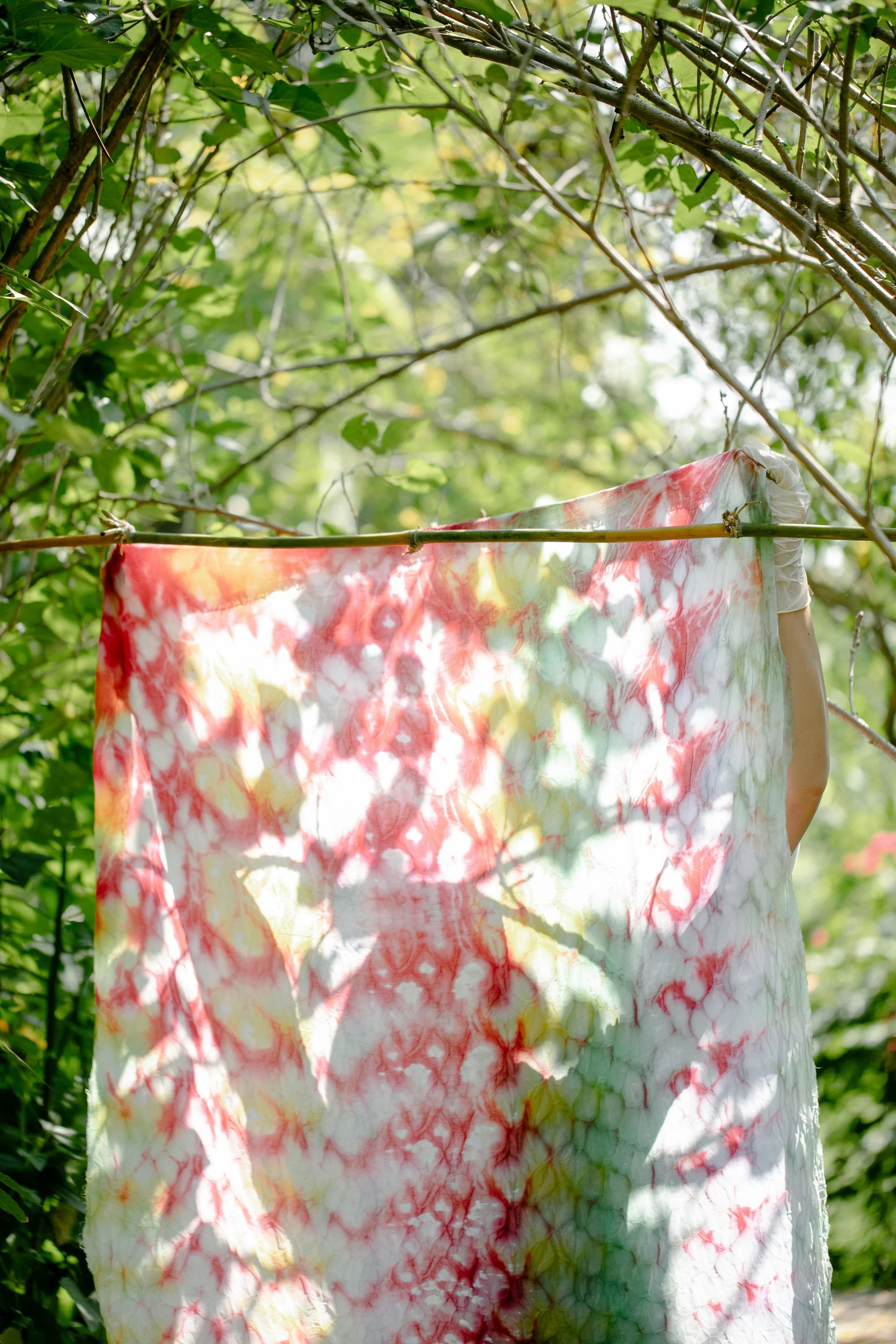 Tissu tie-dye shibori suspendu à une corde dans un environnement extérieur verdoyant.