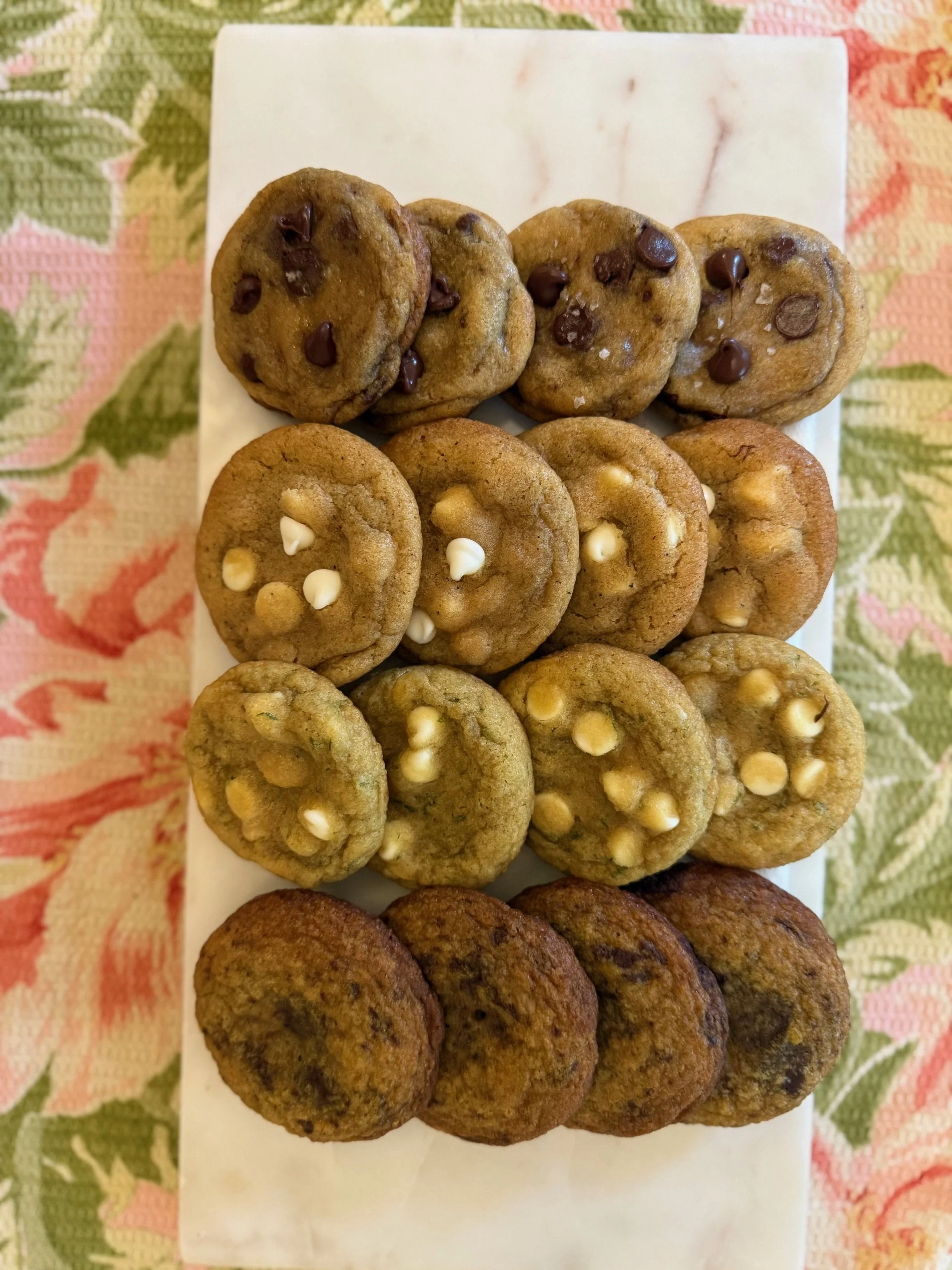 A white rectangular plate holding three types of cookies, placed on a colorful floral tablecloth.
