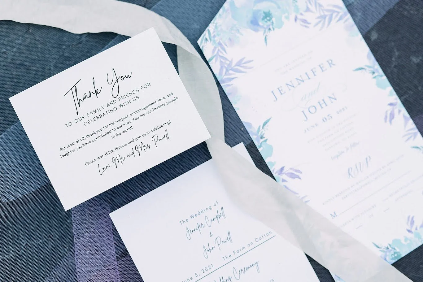 Wedding invitation and thank you card on a dark textured surface, with floral printed invitation and handwritten details.
