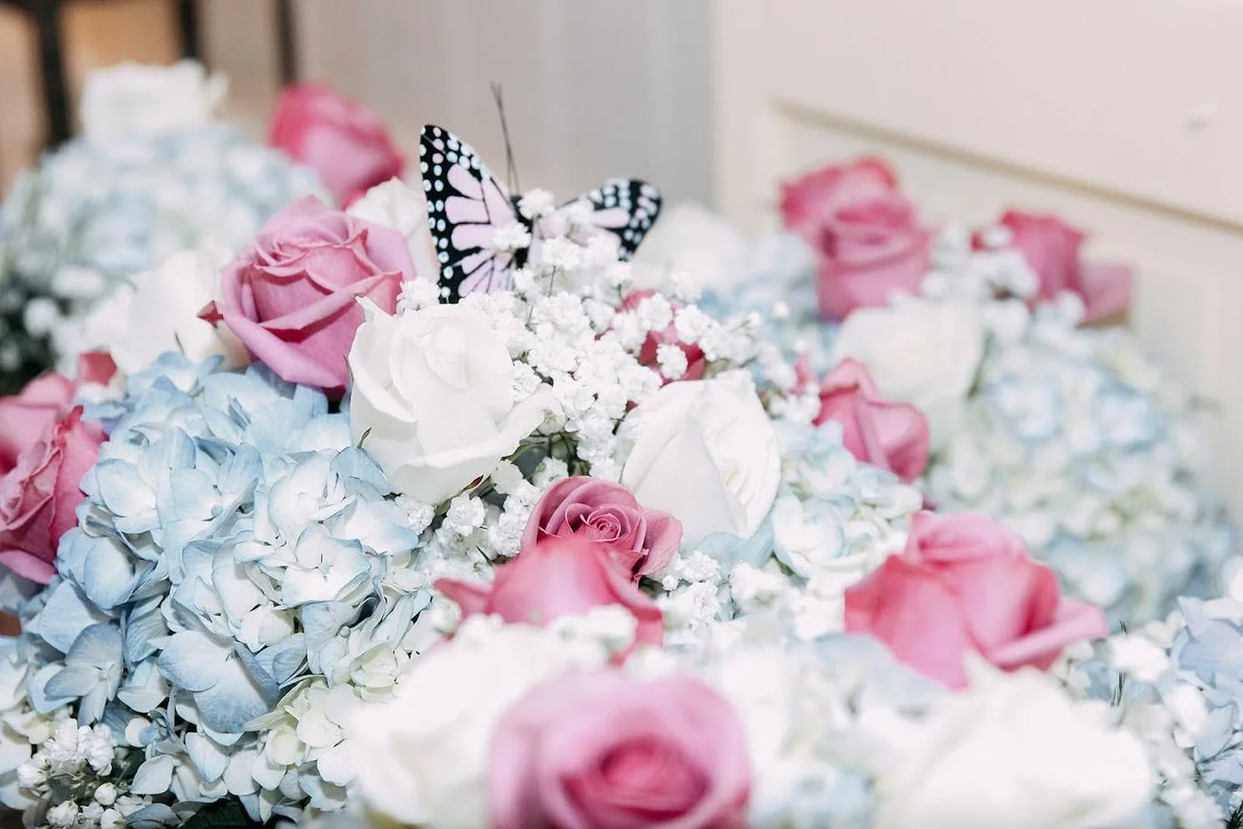 A floral arrangement with pink, white, and light blue flowers, including a butterfly decoration.