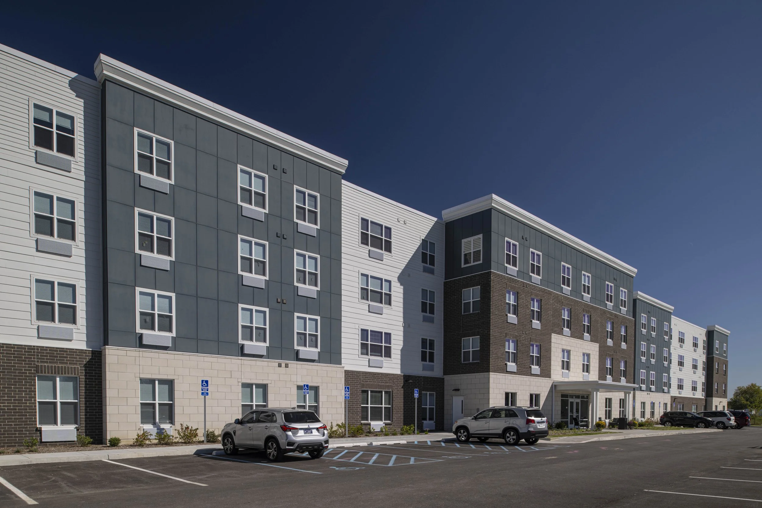Exterior view of a modern multi-story apartment complex with parking lot and cars.