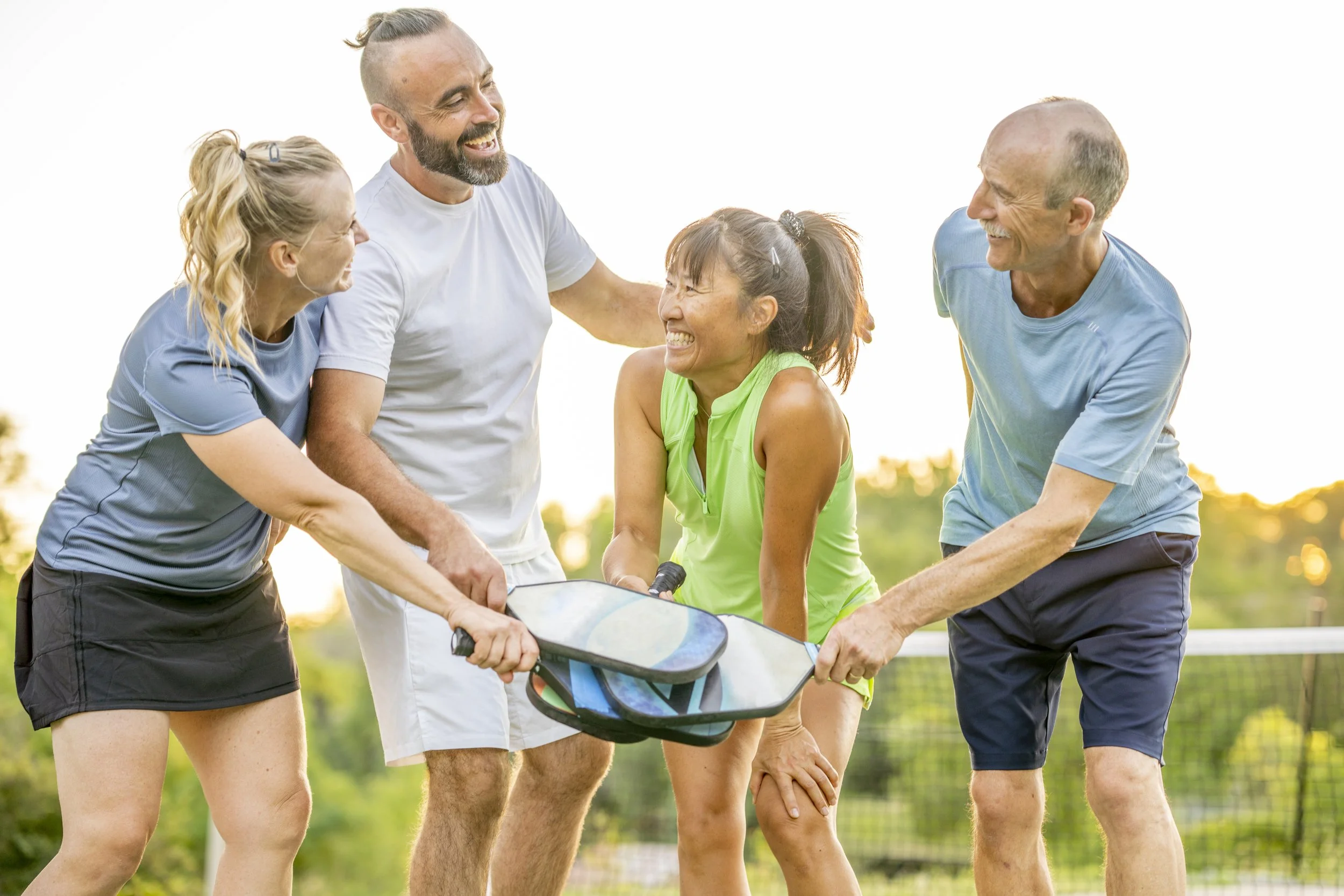 Five friends joyfully playing volleyball outdoors in a park, smiling and holding a volleyball with a net in the background during sunset.