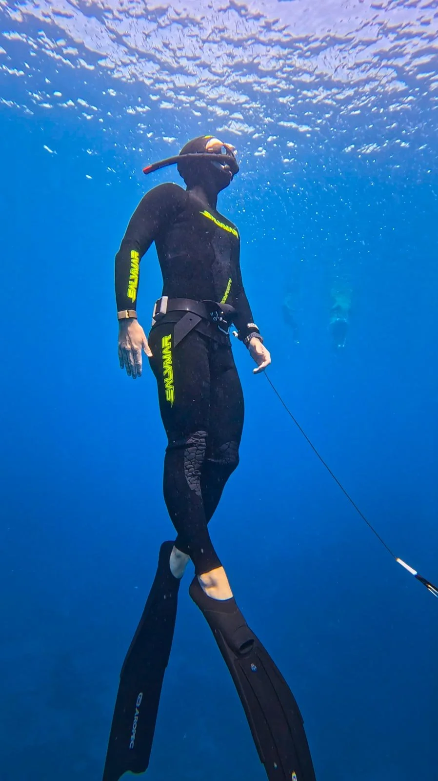 freediver ascending from deep blue water wearing long fins and wetsuit