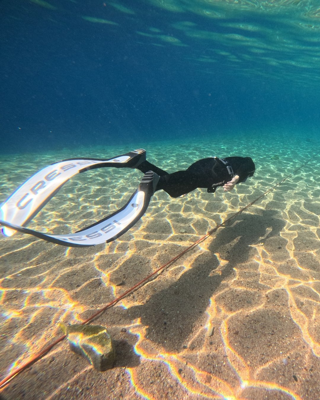 An underwater photo a freediver doing dynamic apnea in the sea against sandy ocean bed.
