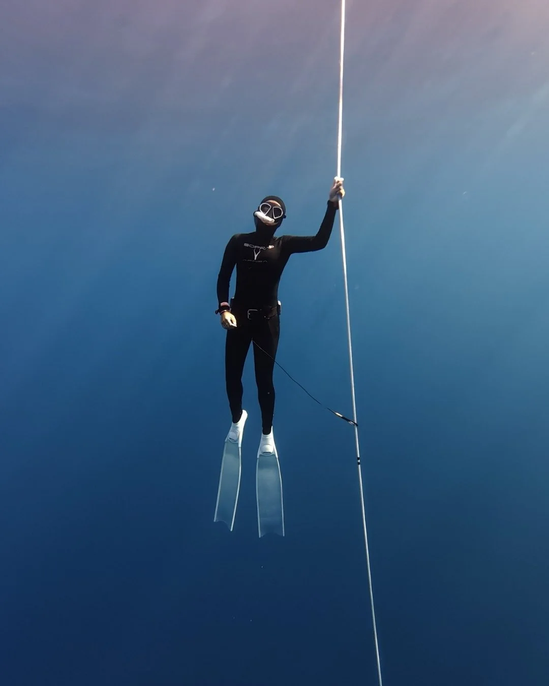 Person in freediving gear with long fins pulling up the rope towards the surface.