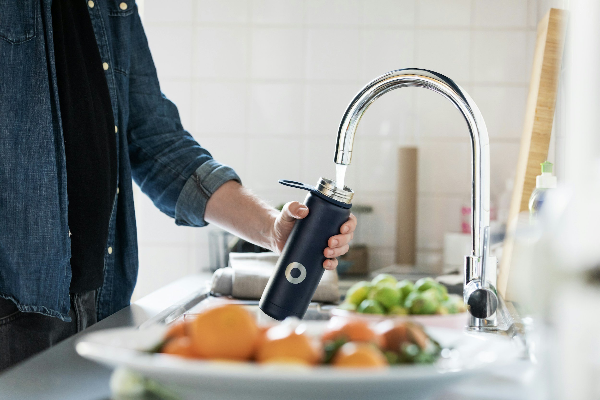 Person filling a water bottle at a kitchen sink with a modern chrome faucet.