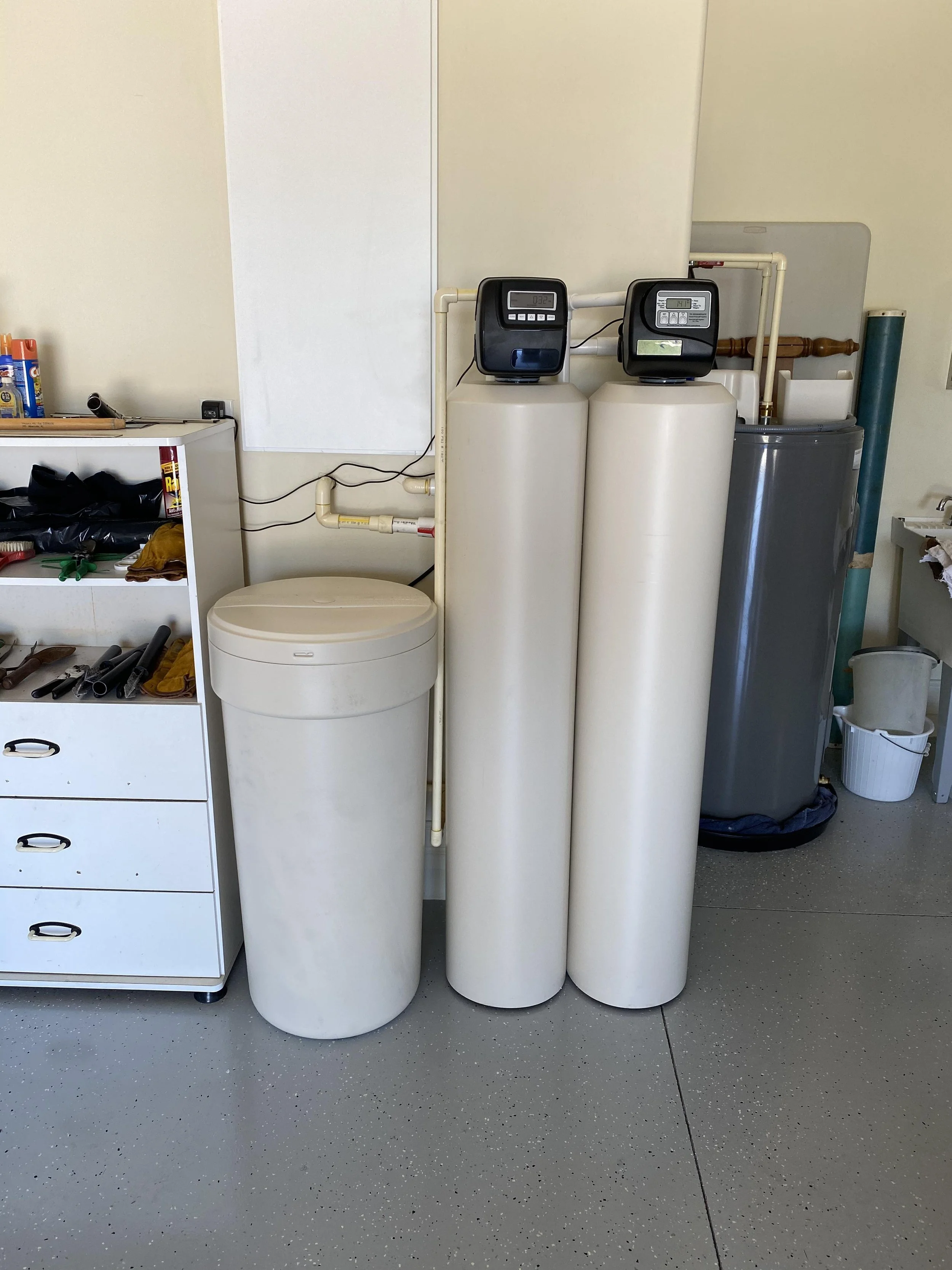A garage with two water treatment tanks, a smaller salt holding tank to the left.