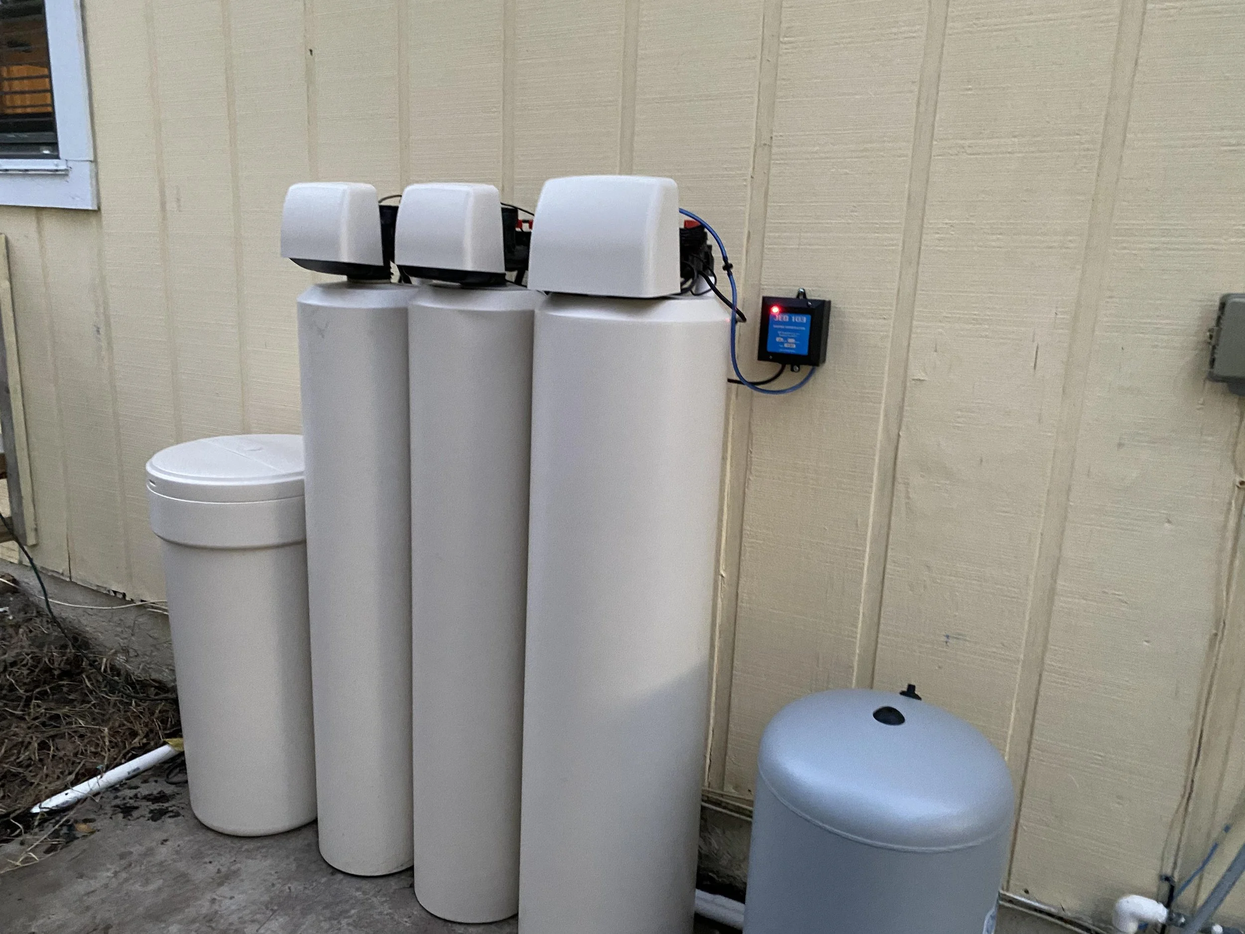 Water filtration system with three tan cylindrical filter units and an ozone unit attached to the wall.