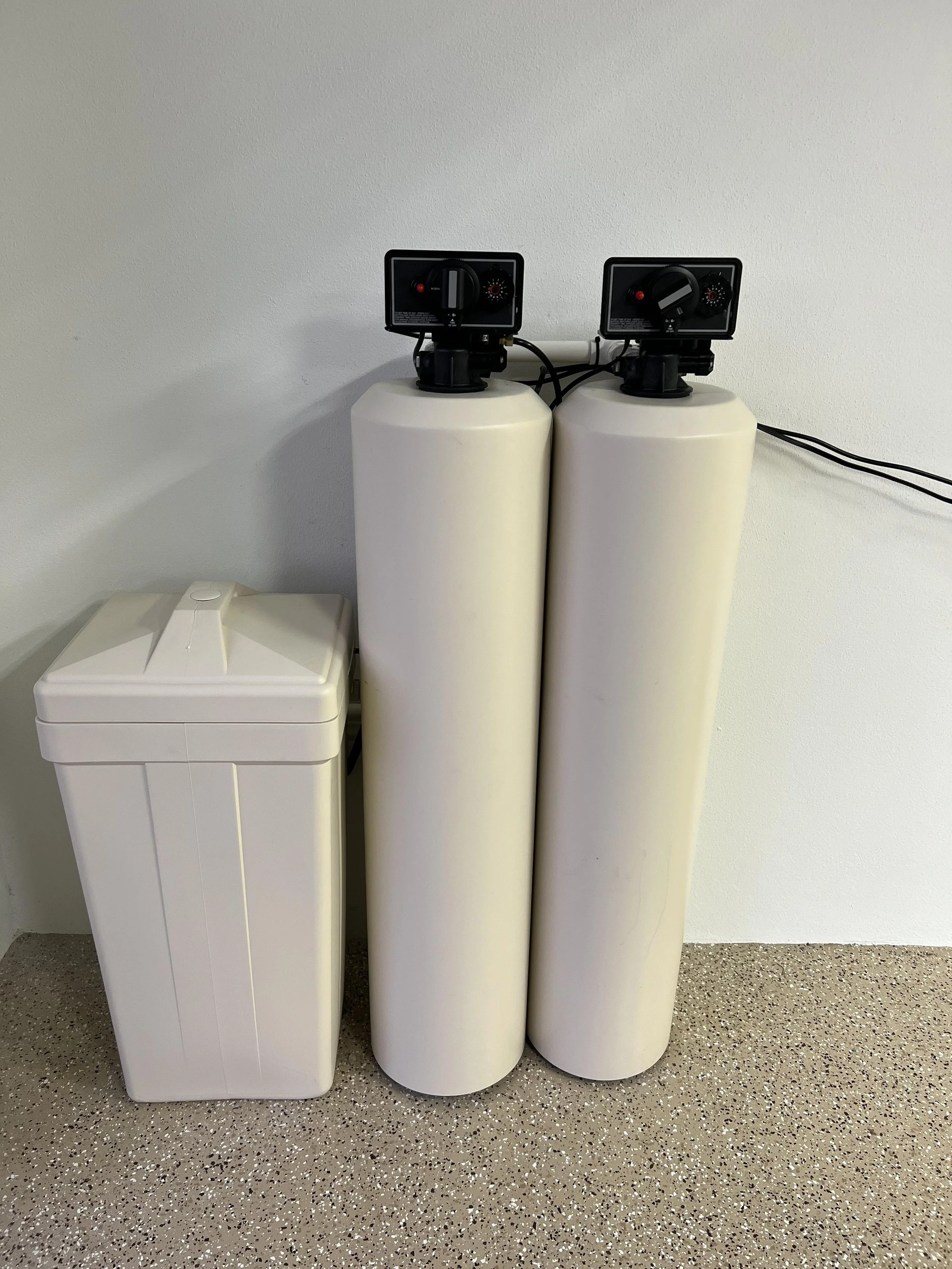 Water softener tanks and control heads in a utility room.