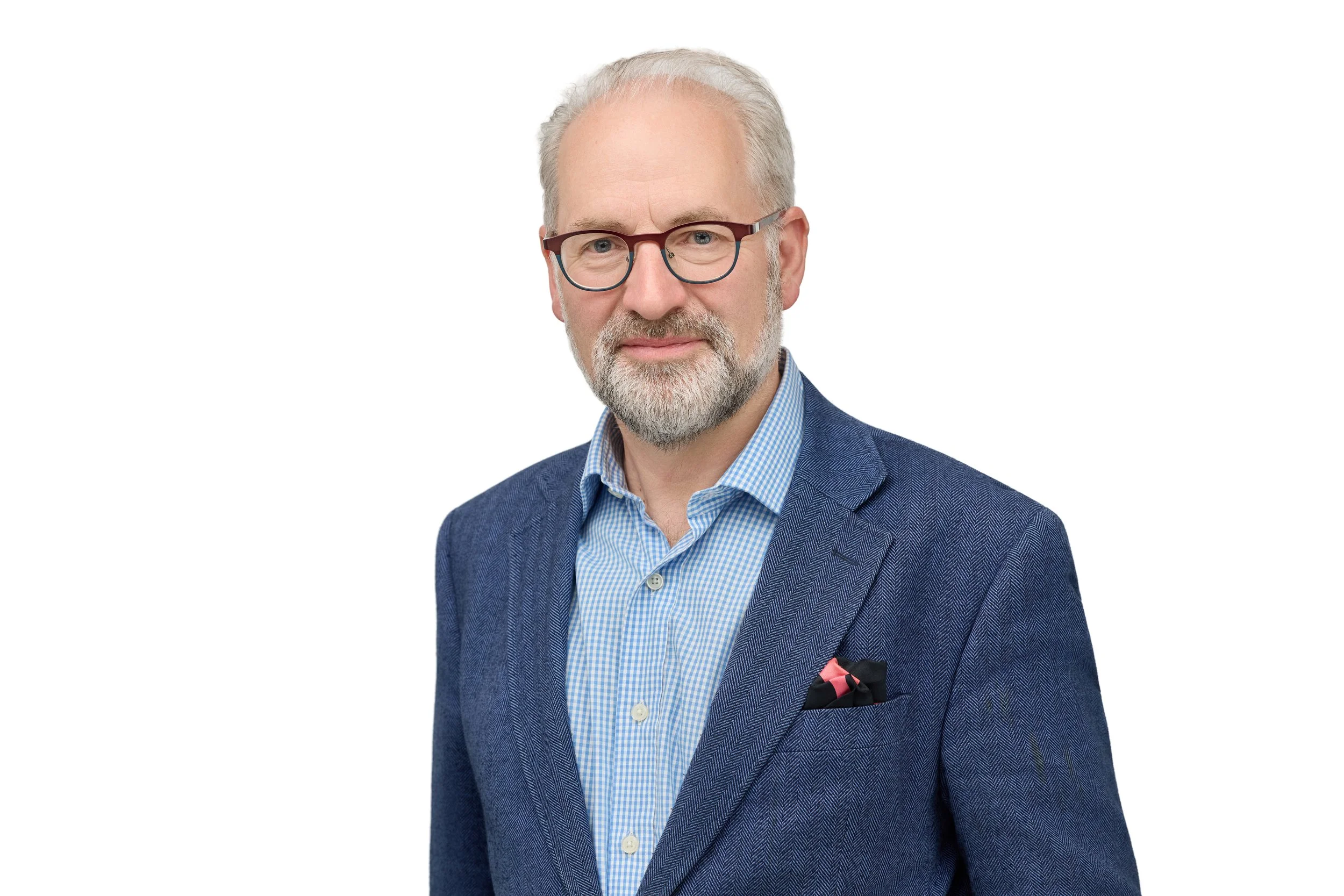 A middle-aged man with gray hair, beard, and glasses wearing a blue blazer, light blue checkered shirt, and pocket square, standing against a plain white background.